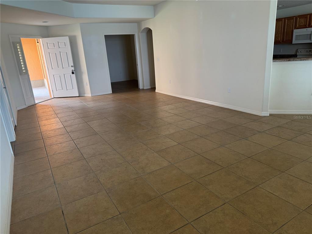 An open living area features tan tile flooring, white walls, and an adjacent kitchen — 3939 SERENADE LANE UNIT 513, LAKELAND, FL