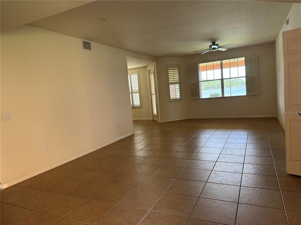 An empty room with tan tile flooring, a ceiling fan, and a view of water — 3939 SERENADE LANE UNIT 513, LAKELAND, FL