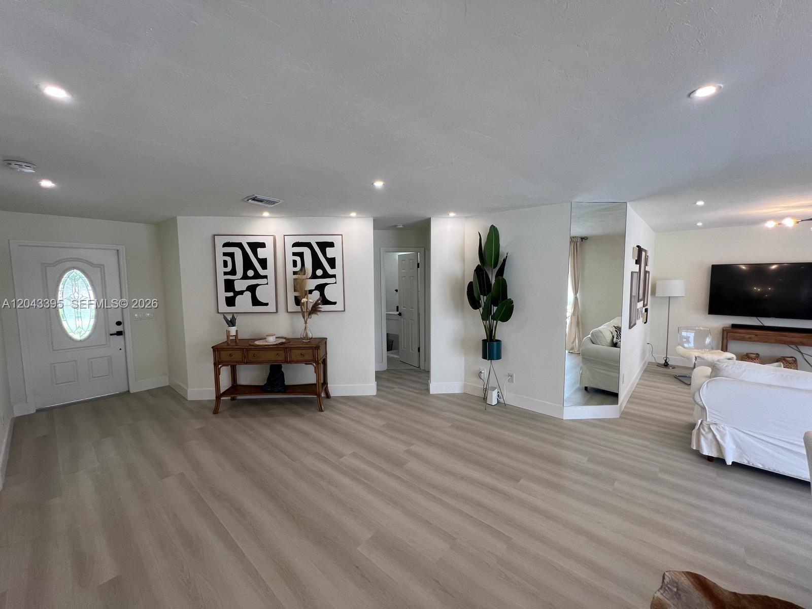 A living room features light wood-look flooring, a white front door, and a mirrored wall — 503 Jackson, Lehigh Acres FL 33972, LEHIGH ACRES, FL