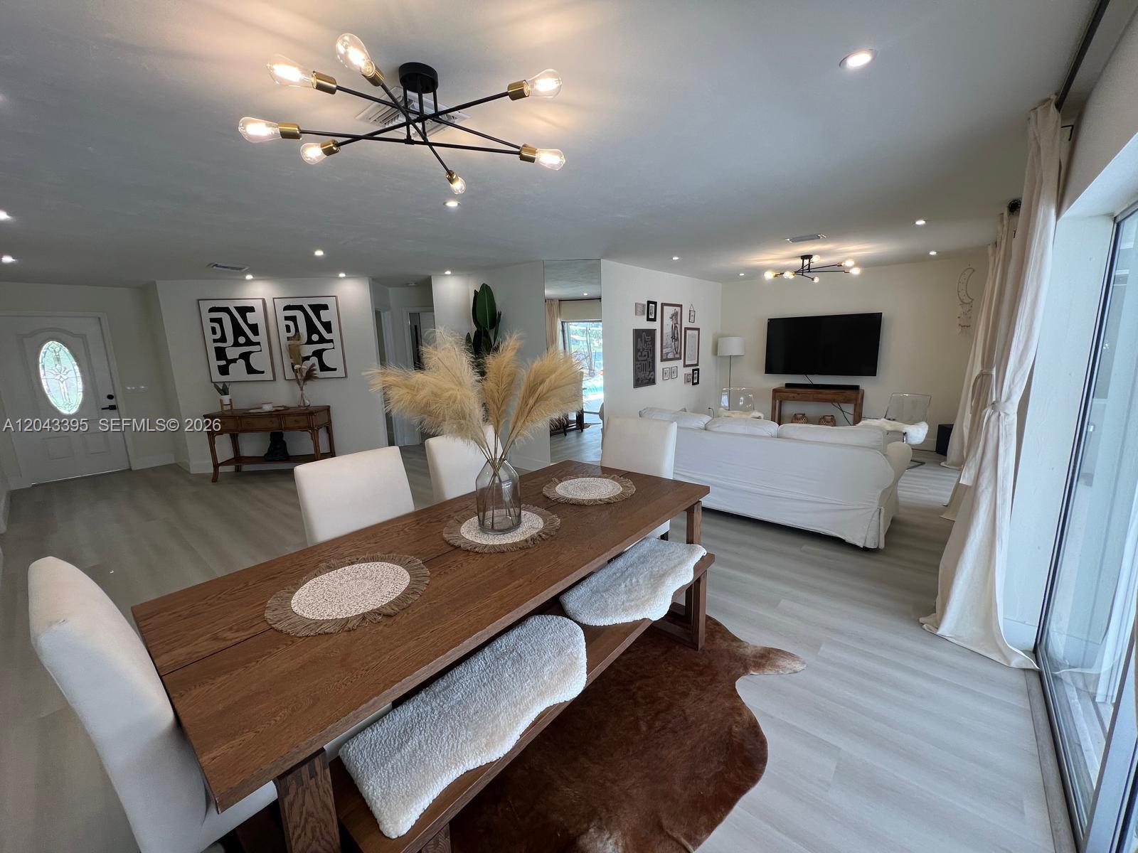 A dining area with a wooden table and bench sits before a living room space — 503 Jackson, Lehigh Acres FL 33972, LEHIGH ACRES, FL