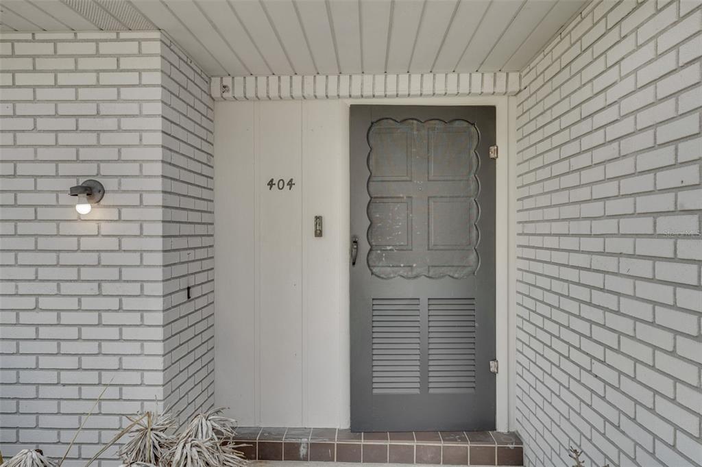 A front entryway features a gray storm door, white brick walls, and the number 404 — 404 LAKE NED ROAD, WINTER HAVEN, FL