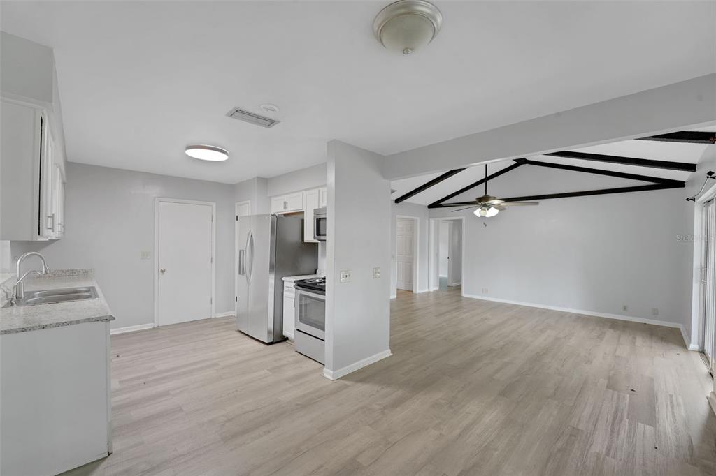 A kitchen with stainless steel appliances and light wood flooring opens into a living area — 404 LAKE NED ROAD, WINTER HAVEN, FL