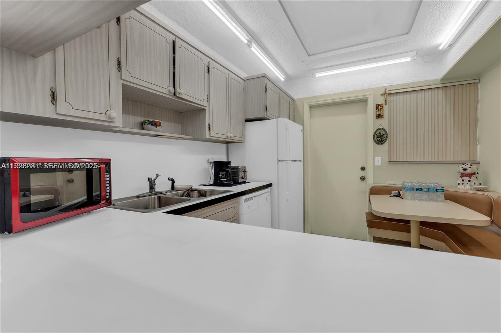 A kitchen features light wood cabinets, white countertops, a red microwave, and a dining nook — 215 SE 3rd Ave # 407B, Hallandale Beach FL 33009, HALLANDALE BEACH, FL