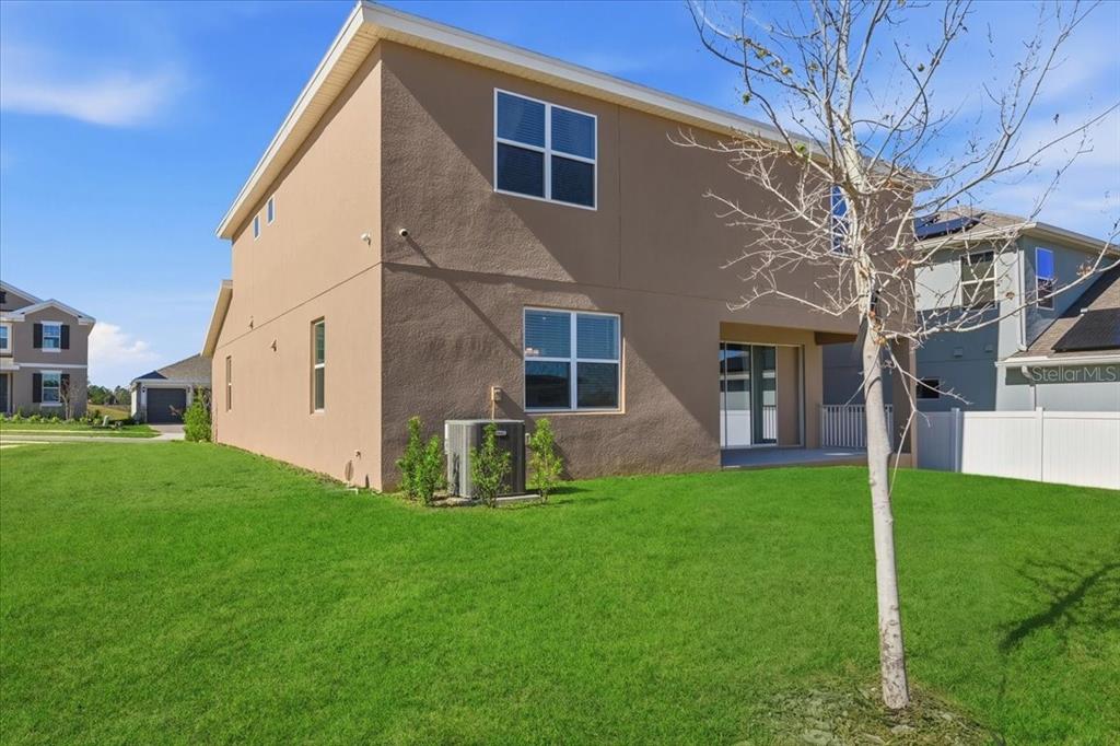 The exterior rear view of a two-story tan house with a grassy backyard — 2072 KEYSTONE PASS BOULEVARD, MINNEOLA, FL