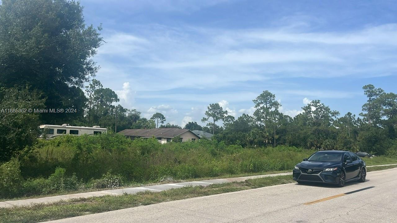 A vacant, overgrown lot features a parked car, a recreational vehicle, and nearby residential houses — 805 E 6 st, Lehigh Acres FL 33972, LEHIGH ACRES, FL