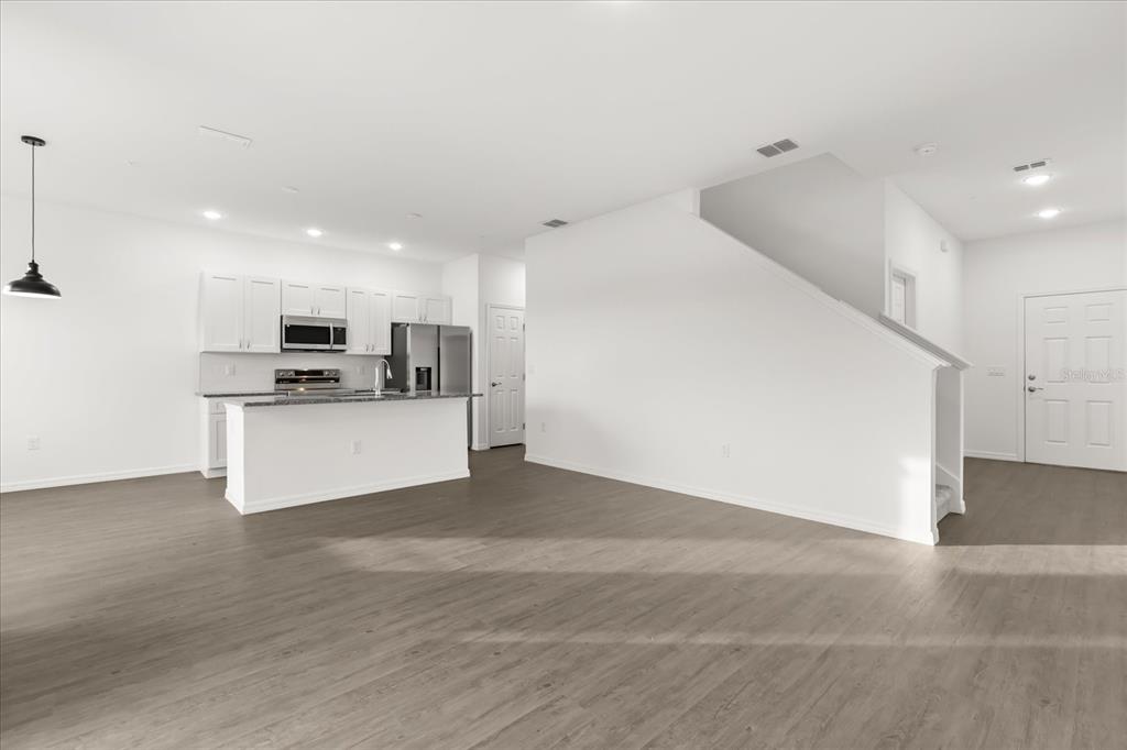 An open-concept kitchen with white cabinets and a center island overlooks a spacious living area — 915 LAKEFRONT VILLAGE DRIVE, CLERMONT, FL