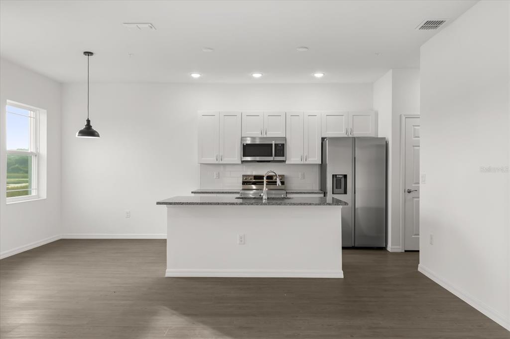 A modern kitchen features white cabinets, stainless steel appliances, a granite island, and wood-look flooring — 915 LAKEFRONT VILLAGE DRIVE, CLERMONT, FL