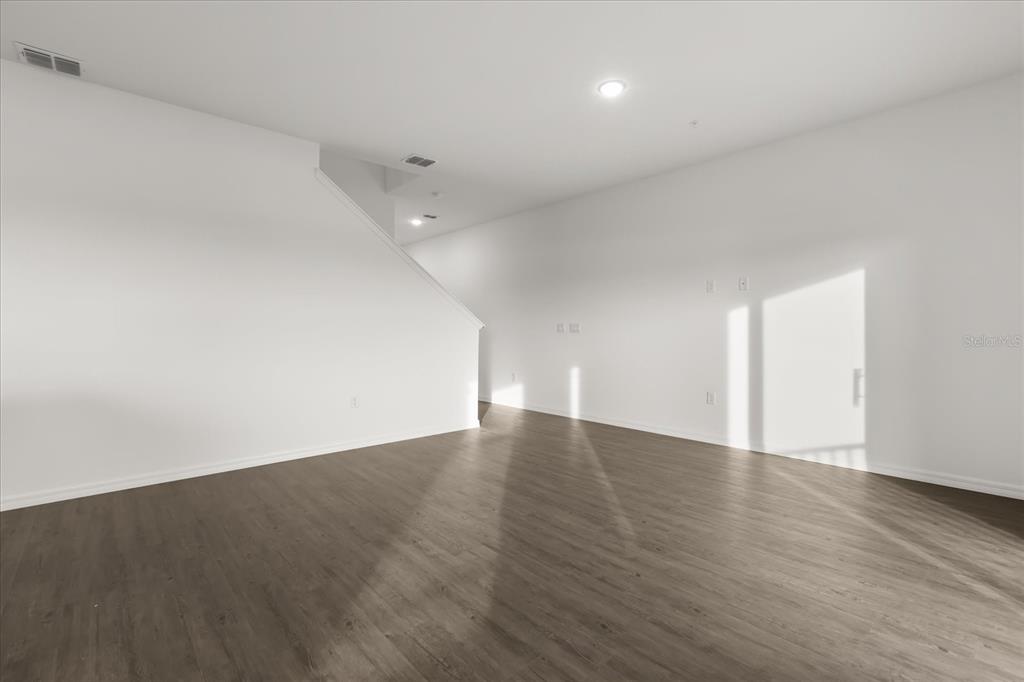 An empty living room features white walls, wood-look flooring, and a staircase — 915 LAKEFRONT VILLAGE DRIVE, CLERMONT, FL