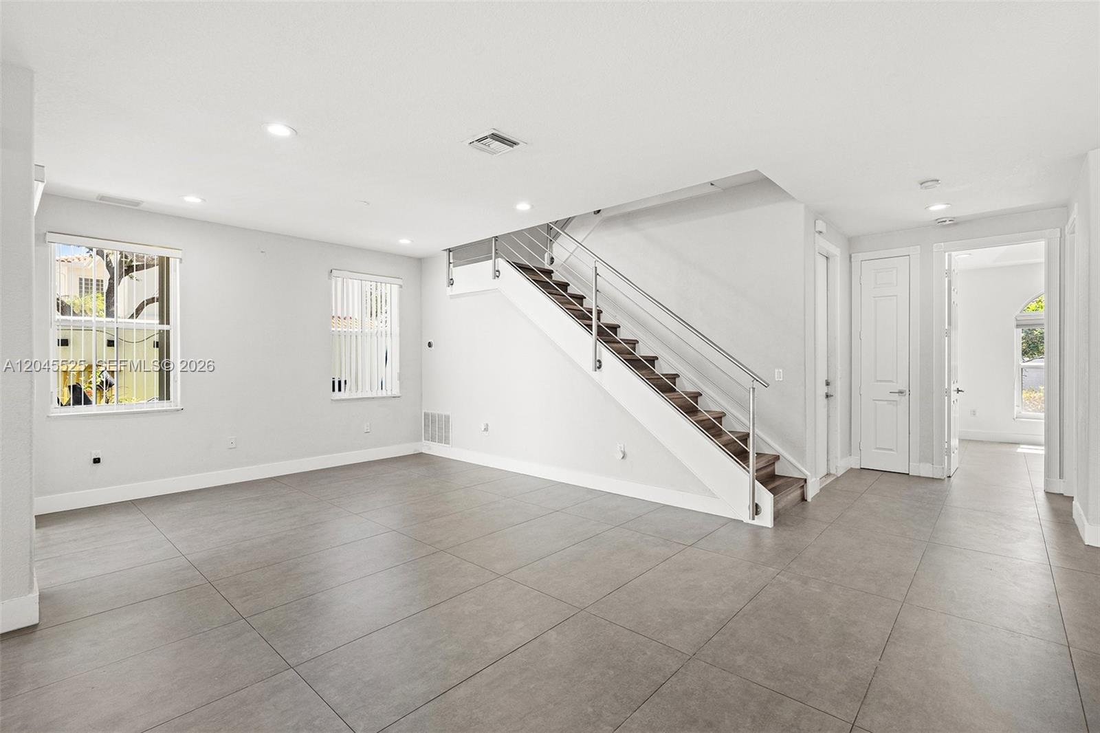 An empty living room features large gray floor tiles, white walls, and a modern staircase — 1549 Shoreline Way, Hollywood FL 33019, HOLLYWOOD, FL