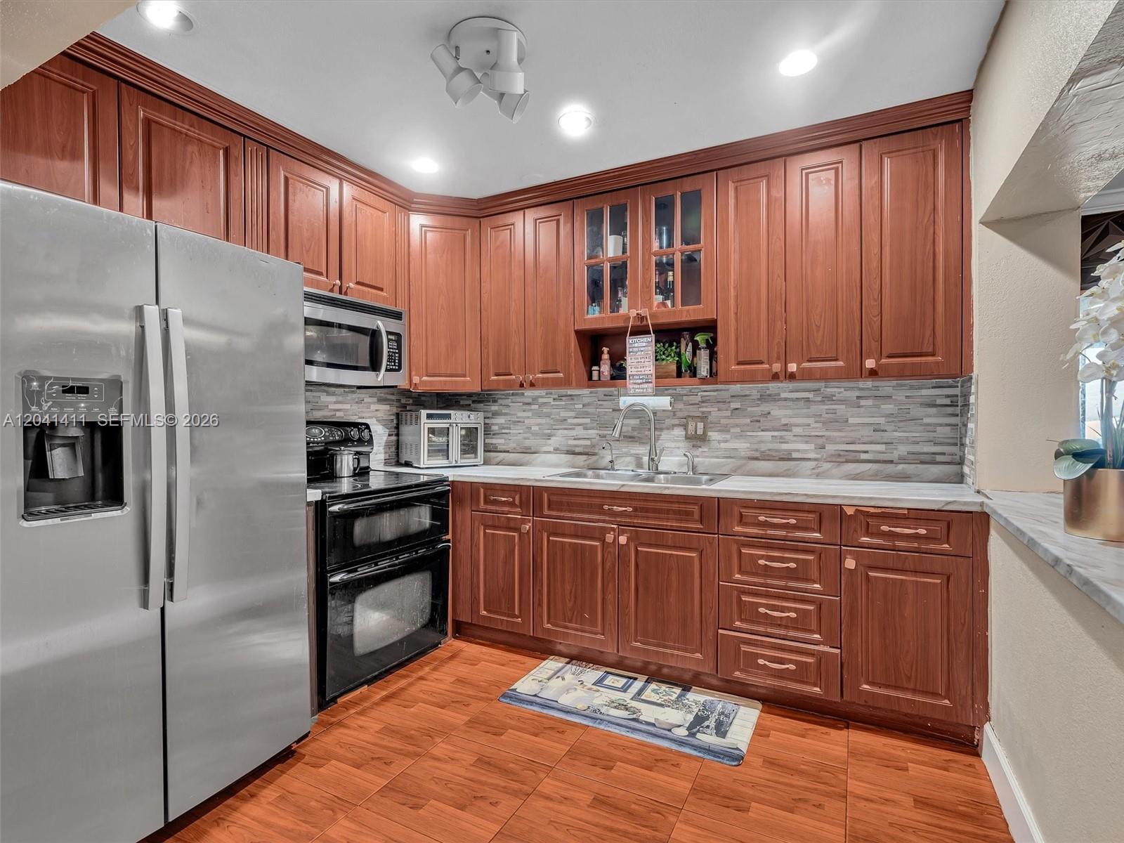 A kitchen features wood cabinets, stainless steel appliances, a tiled backsplash, and wood-look flooring — 19100 NW 51st Ave, Unincorporated Dade County FL 33055, UNINCORPORATED DADE COUNTY, FL