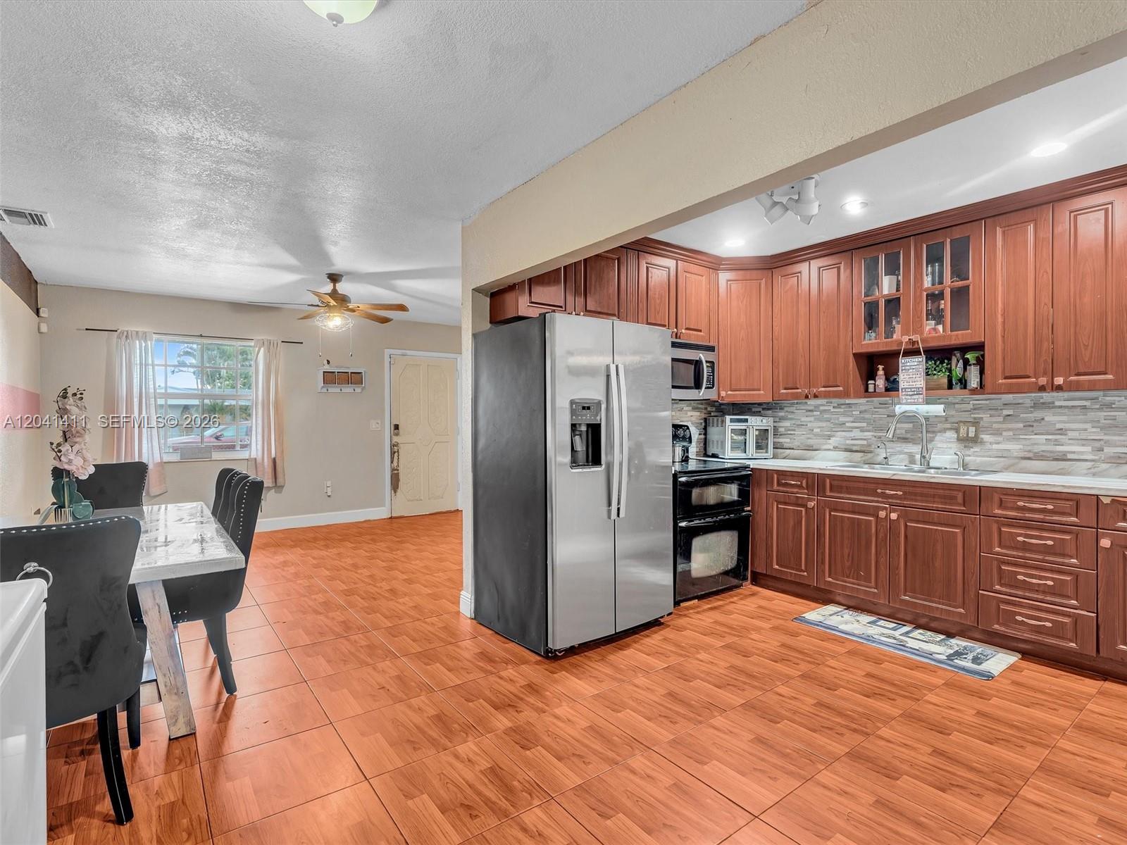 An open-concept kitchen and dining area features wood-look tile flooring and cherry-toned cabinetry — 19100 NW 51st Ave, Unincorporated Dade County FL 33055, UNINCORPORATED DADE COUNTY, FL