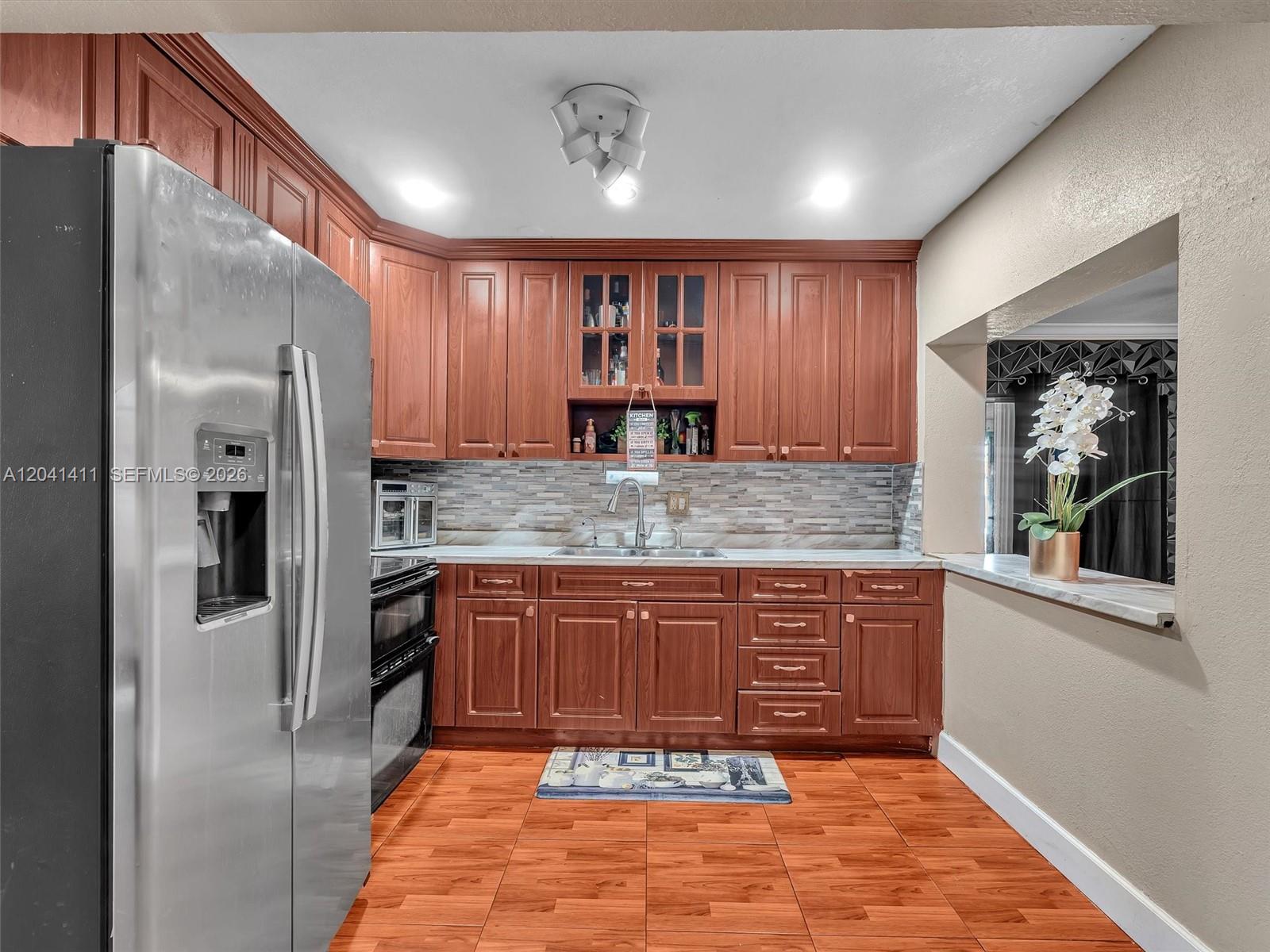 A kitchen features wood cabinets, stainless steel appliances, a tiled backsplash, and wood-look floor tiles — 19100 NW 51st Ave, Unincorporated Dade County FL 33055, UNINCORPORATED DADE COUNTY, FL