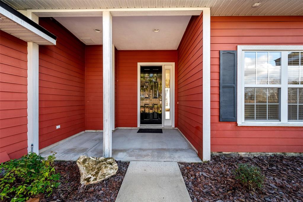 A front porch with a black door, red horizontal siding, and a concrete walkway — 10215 SW 98 TH AVENUE, GAINESVILLE, FL