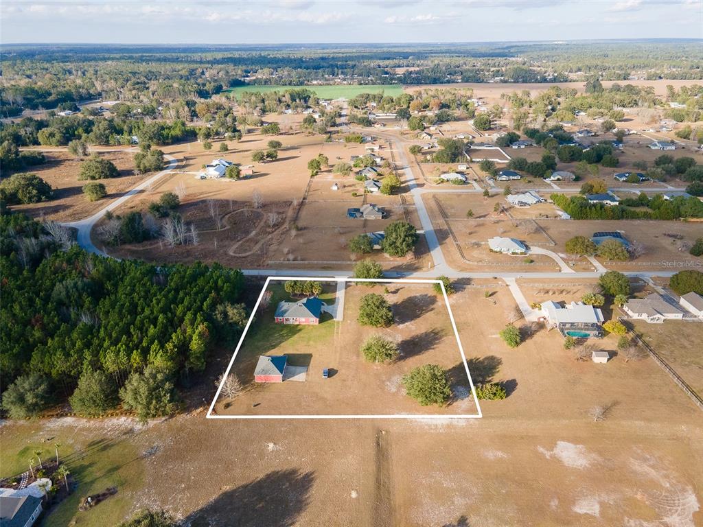 An aerial view shows a residential property with a house and detached garage on land — 10215 SW 98 TH AVENUE, GAINESVILLE, FL