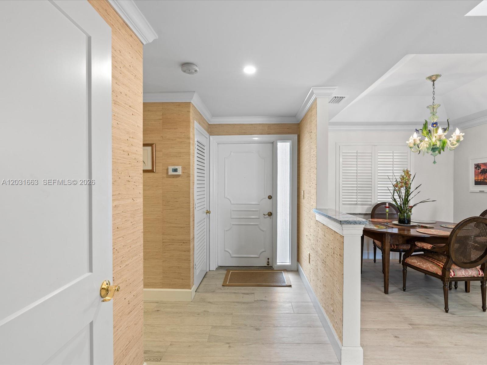 An entryway with textured wallpaper leads to a dining area featuring a decorative chandelier — 2160 Ibis Isle Rd # 3, Palm Beach FL 33480, PALM BEACH, FL