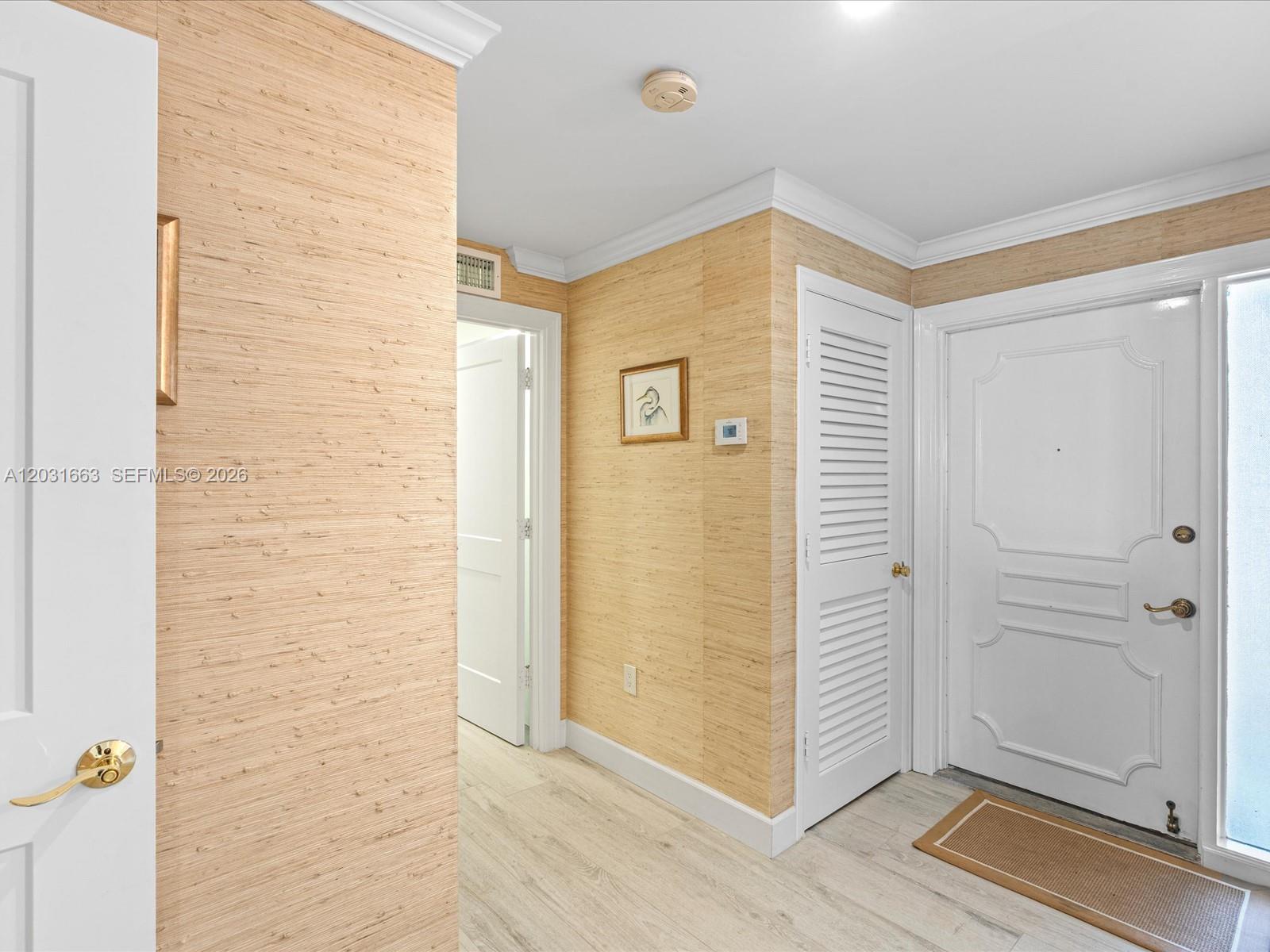 An entryway features light wood-look flooring, textured beige wallpaper, and white paneled doors — 2160 Ibis Isle Rd # 3, Palm Beach FL 33480, PALM BEACH, FL