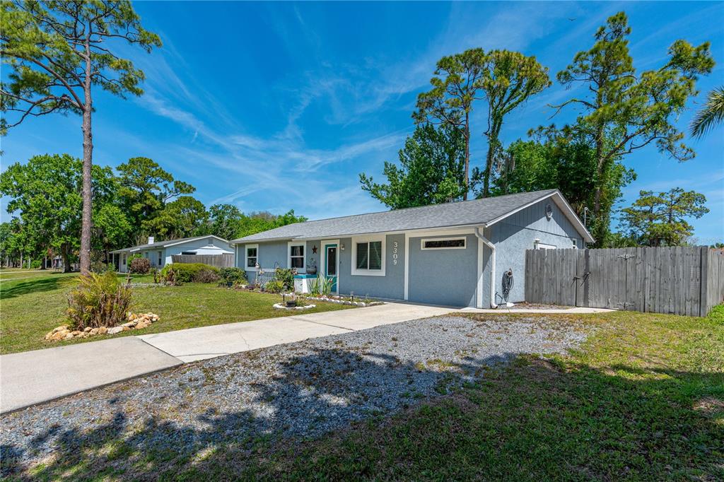 A single-story light blue house with a gravel driveway and a wooden fence — 3309 WOODLAND DRIVE, EDGEWATER, FL