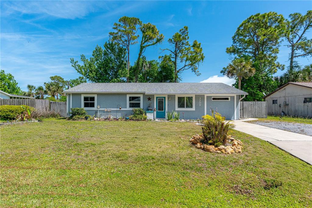 A single-story gray house with a teal front door and a concrete driveway — 3309 WOODLAND DRIVE, EDGEWATER, FL