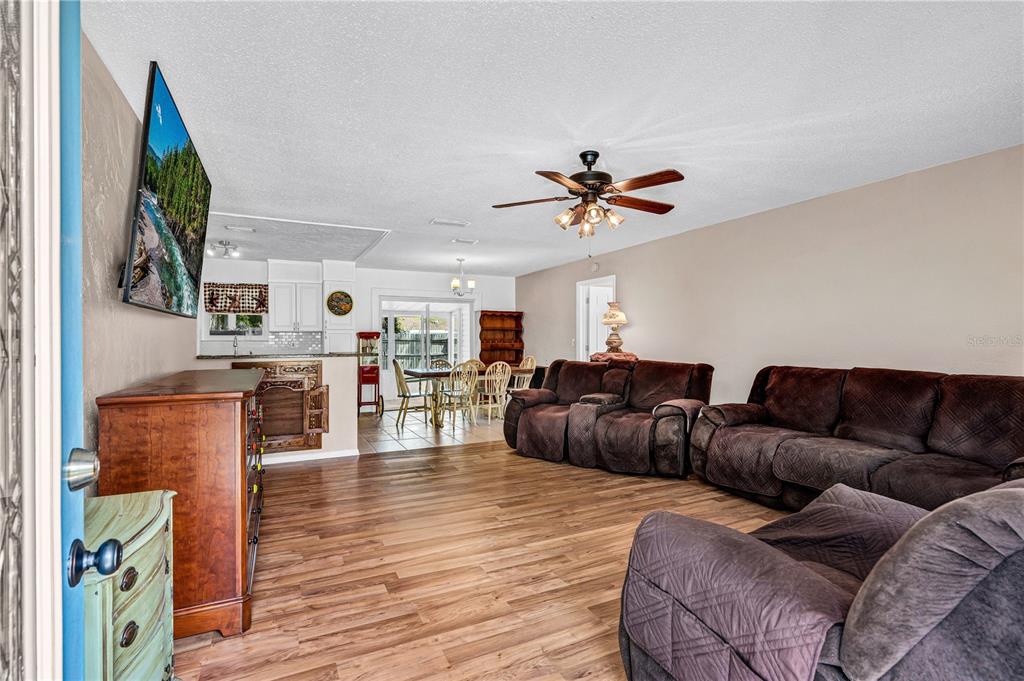 A living room with wood-look flooring, brown reclining furniture, and an open dining area — 3309 WOODLAND DRIVE, EDGEWATER, FL