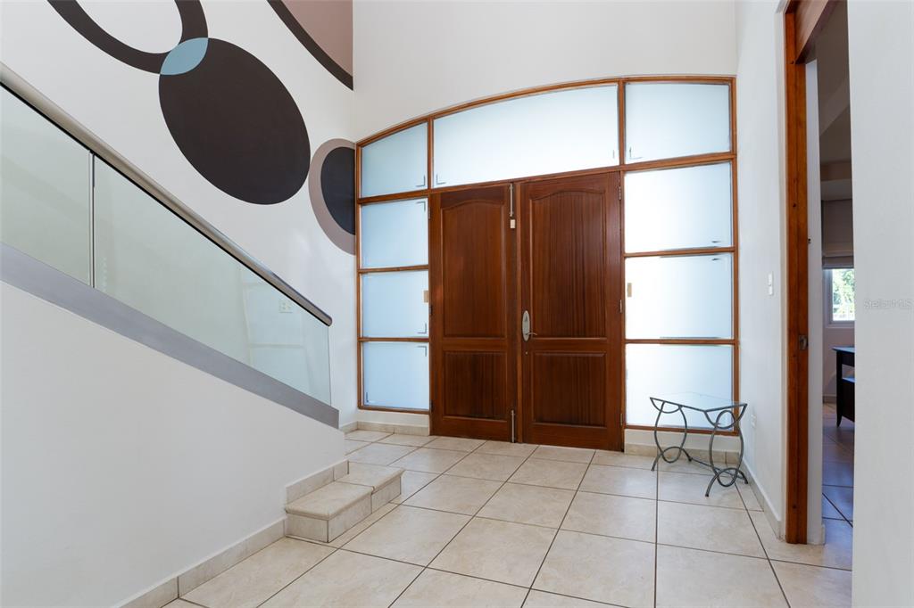A tiled entryway features double wooden doors, frosted glass panels, and a glass-railed staircase — 797 MAR DE CASPIO, DORADO, PR
