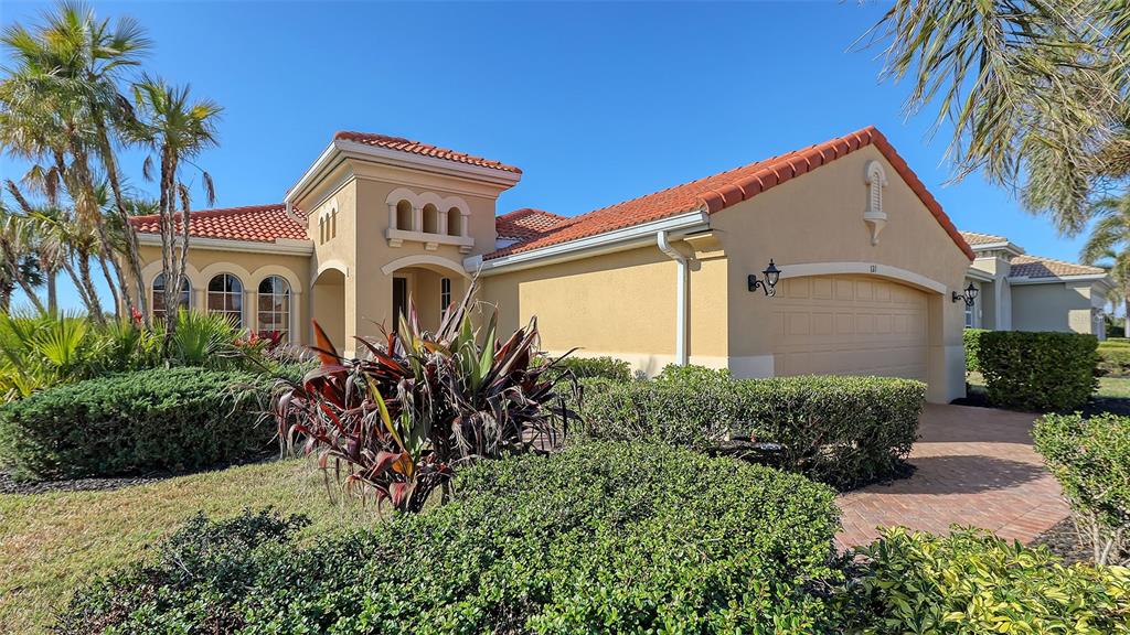 A single-story house with a tan stucco exterior, red tile roof, and a two-car garage — 121 SAVONA WAY, NOKOMIS, FL