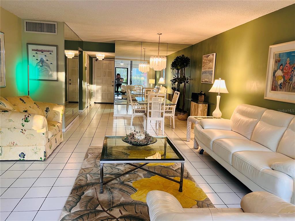A living and dining room with white tile floors, mirrored walls, and green accent walls — 4387 TREVI COURT UNIT 107, LAKE WORTH, FL