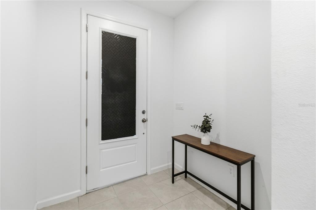 A white front door with a dark glass panel stands beside a narrow console table — 905 HONEY PETAL LANE, DELAND, FL