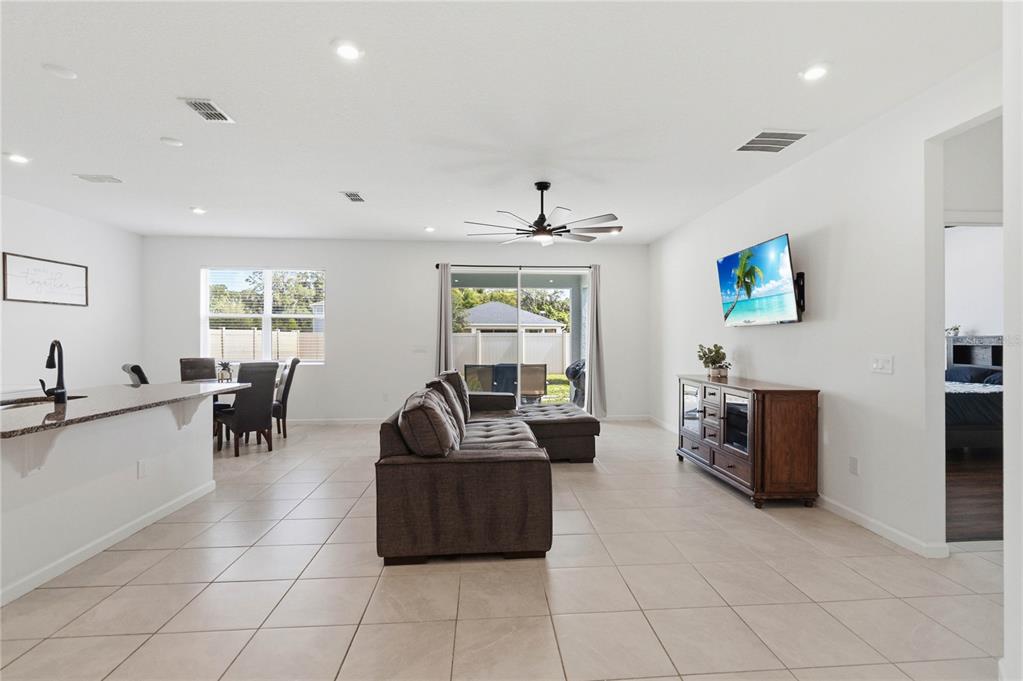 An open-concept living and dining area features tile flooring, a sectional sofa, and a television — 905 HONEY PETAL LANE, DELAND, FL