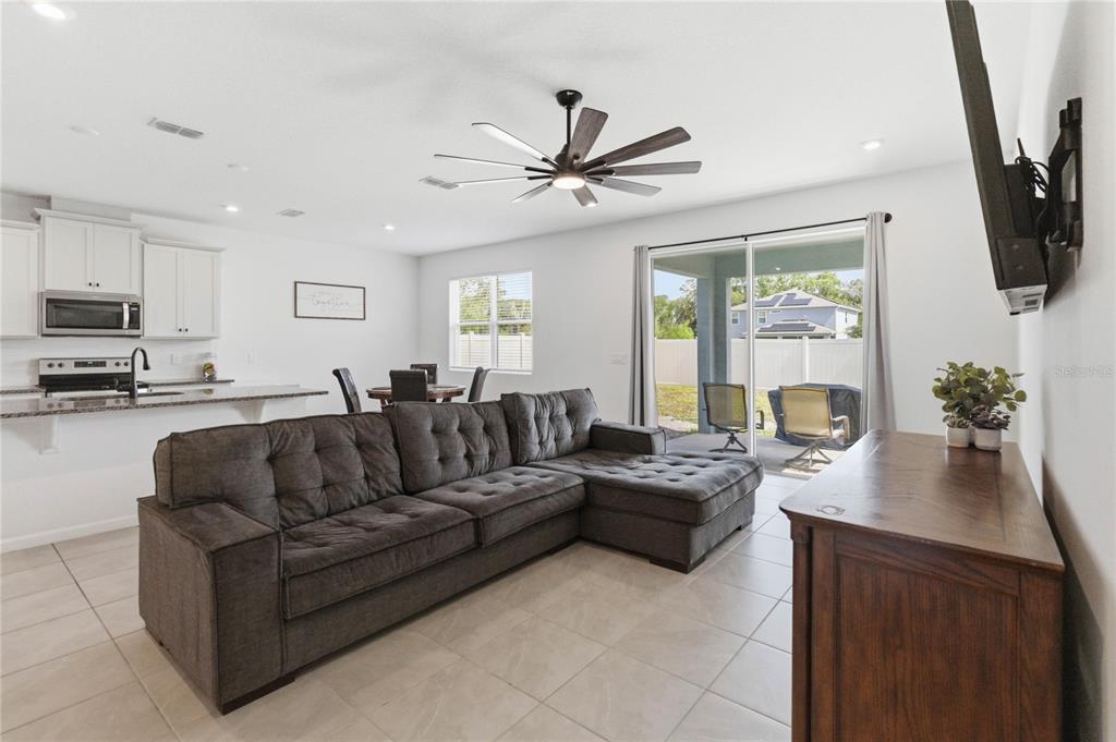A living room with a gray sectional sofa, tile flooring, and a sliding glass door — 905 HONEY PETAL LANE, DELAND, FL