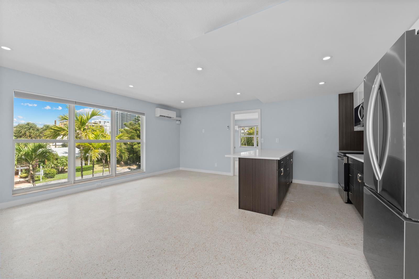 An open-concept kitchen and living area with light-colored flooring, a kitchen island, and large windows — 3220 NE 7th # 2, Pompano Beach FL 33062, POMPANO BEACH, FL