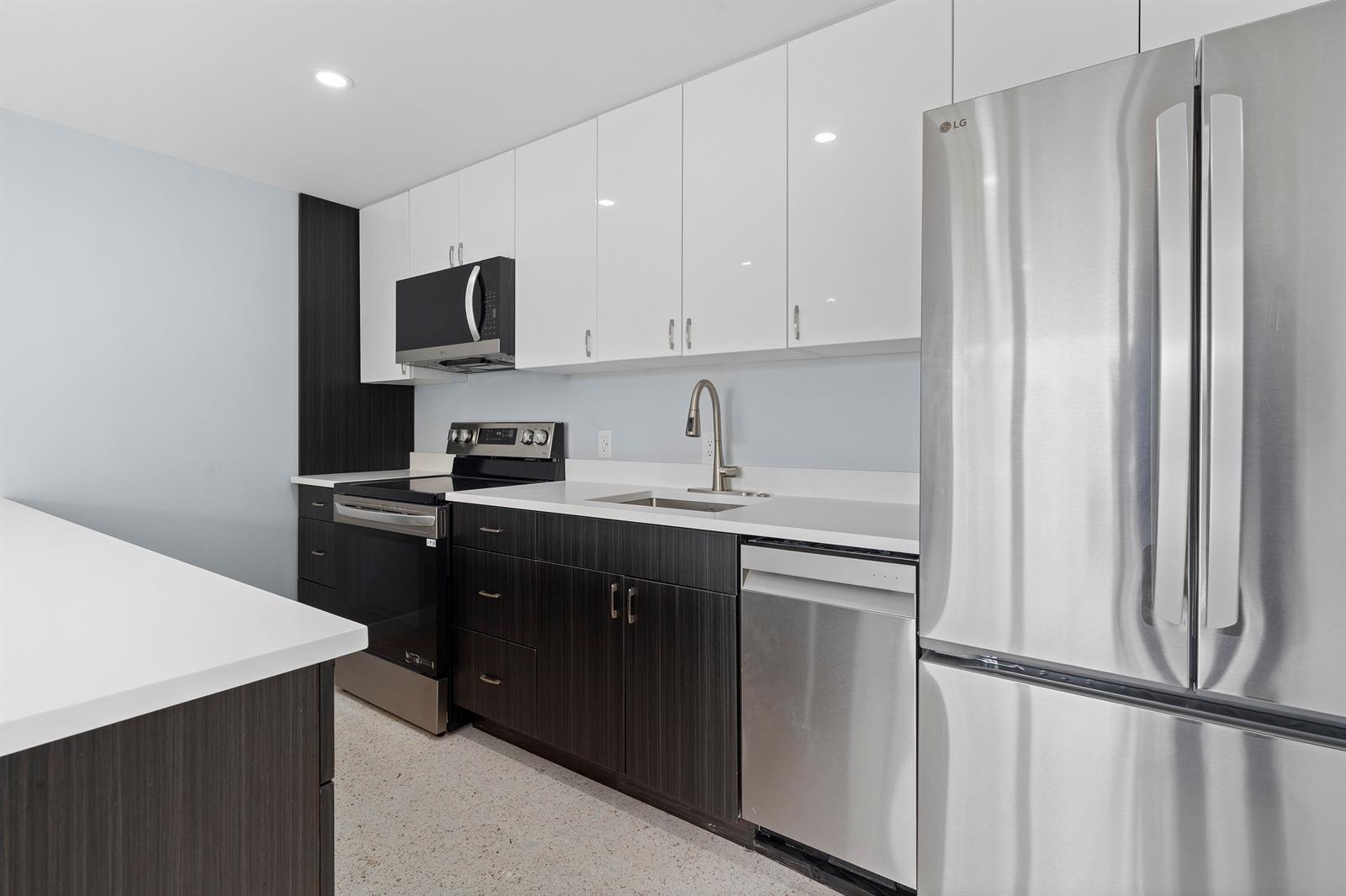A modern kitchen features white upper cabinets, dark lower cabinets, stainless steel appliances, and countertops — 3220 NE 7th # 2, Pompano Beach FL 33062, POMPANO BEACH, FL