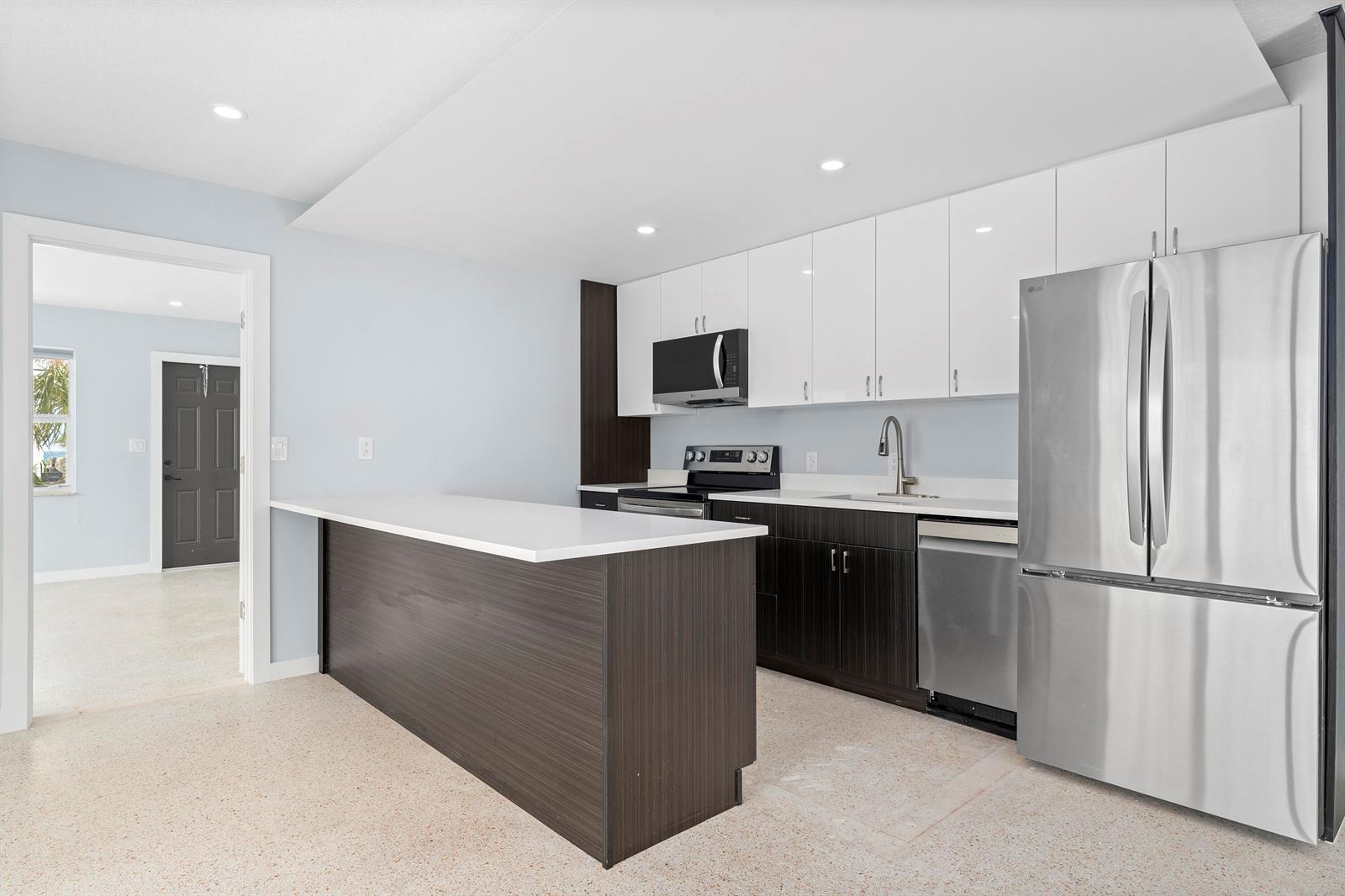 A modern kitchen features dark wood cabinetry, white upper cabinets, stainless steel appliances, and an island — 3220 NE 7th # 2, Pompano Beach FL 33062, POMPANO BEACH, FL