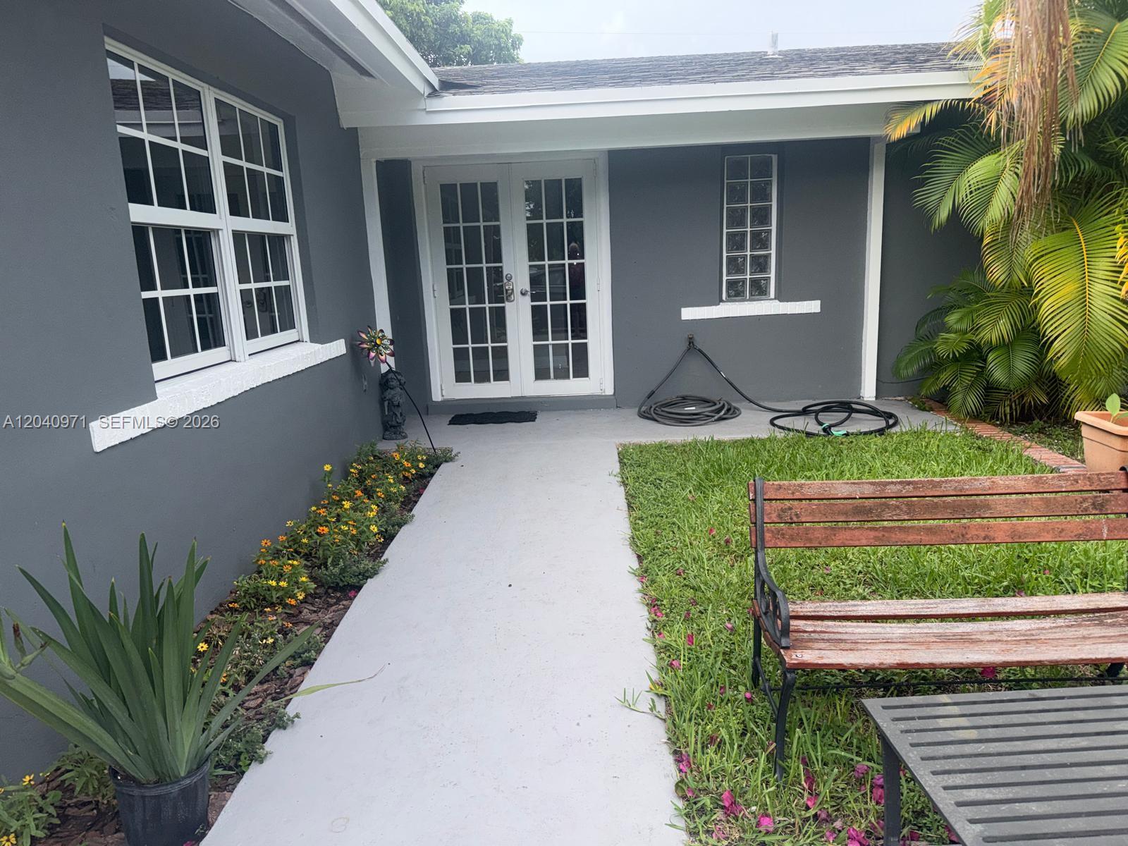 A gray house exterior features a concrete walkway, a wooden bench, and a glass-paned door — 12551 SW 35th St, Miami FL 33175, MIAMI, FL
