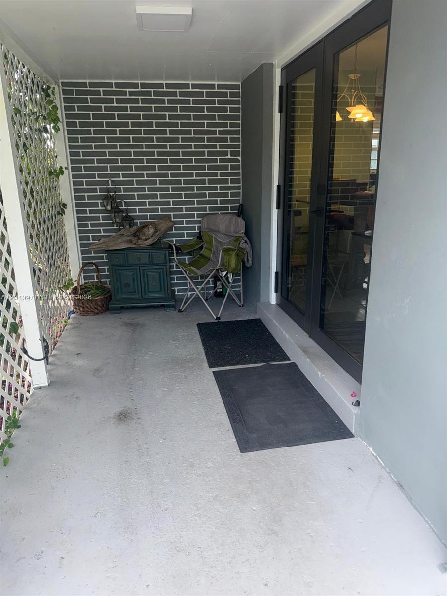 A covered patio features a gray brick wall, a folding chair, and double glass doors — 12551 SW 35th St, Miami FL 33175, MIAMI, FL