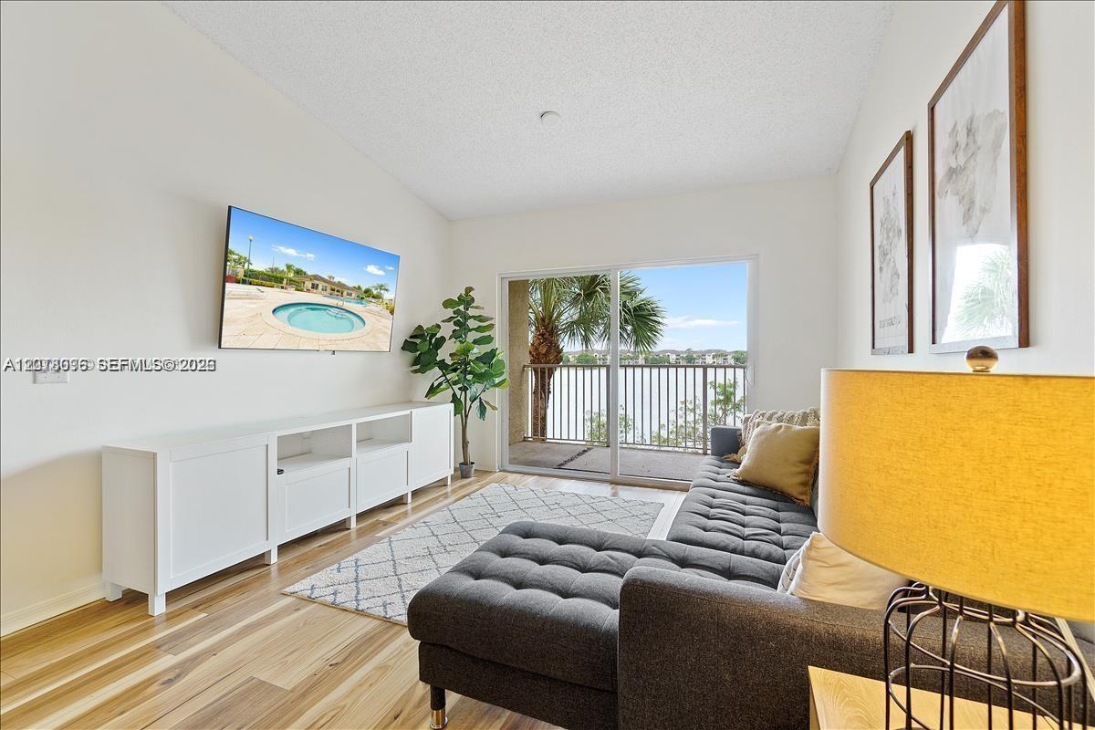 A living room features a gray sectional sofa, a white media console, and a balcony — 5065 Wiles Rd # 308, Coconut Creek FL 33073, COCONUT CREEK, FL