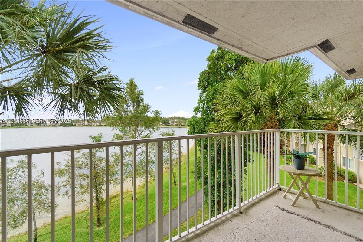 A balcony with a white railing overlooks a lake, palm trees, and green lawn — 5065 Wiles Rd # 308, Coconut Creek FL 33073, COCONUT CREEK, FL