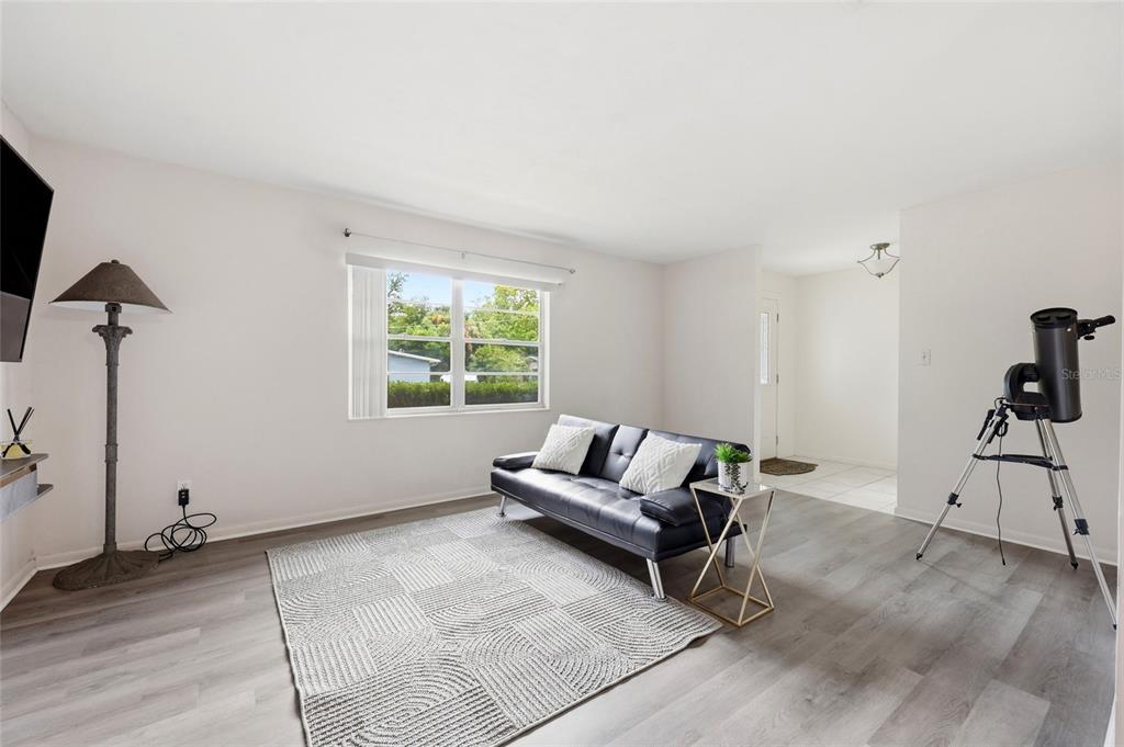 A living room features gray wood-look flooring, a black futon, and a telescope on a tripod — 4628 NW 40TH STREET, GAINESVILLE, FL