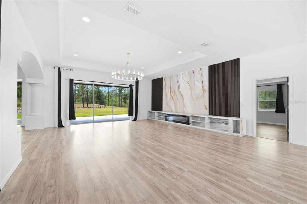 A spacious living room features light wood flooring, a marble fireplace wall, and sliding glass doors — 18043 PALMDALE ROAD, WEEKI WACHEE, FL