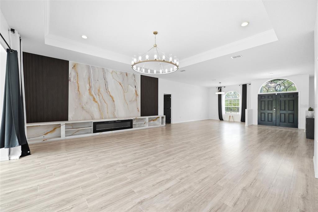 A spacious living room features light wood-look tile flooring, a marble fireplace wall, and chandelier — 18043 PALMDALE ROAD, WEEKI WACHEE, FL