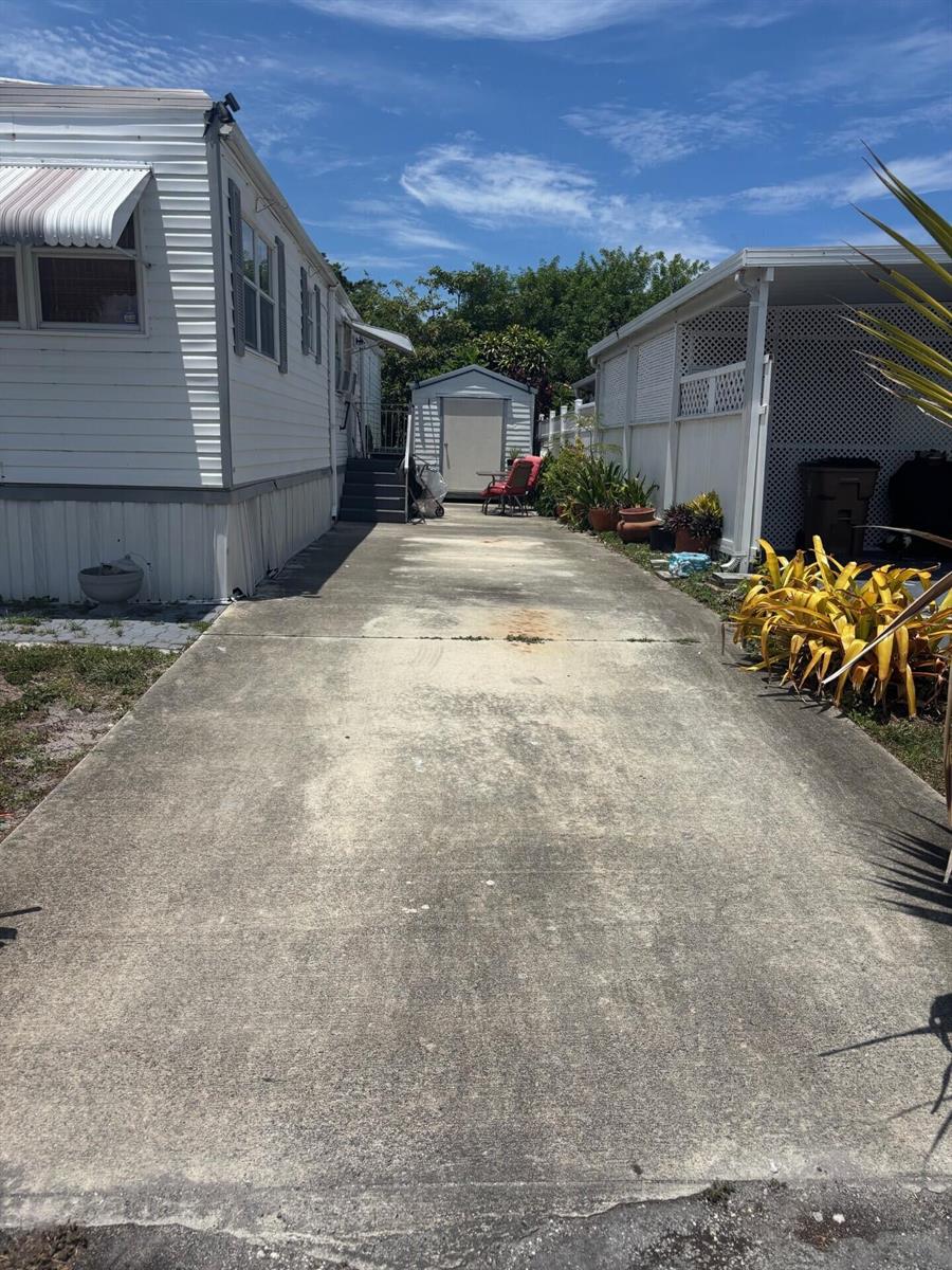A concrete driveway leads between a mobile home and a carport toward a storage shed — 109 NW 50th Street, Deerfield Beach FL 33064, DEERFIELD BEACH, FL
