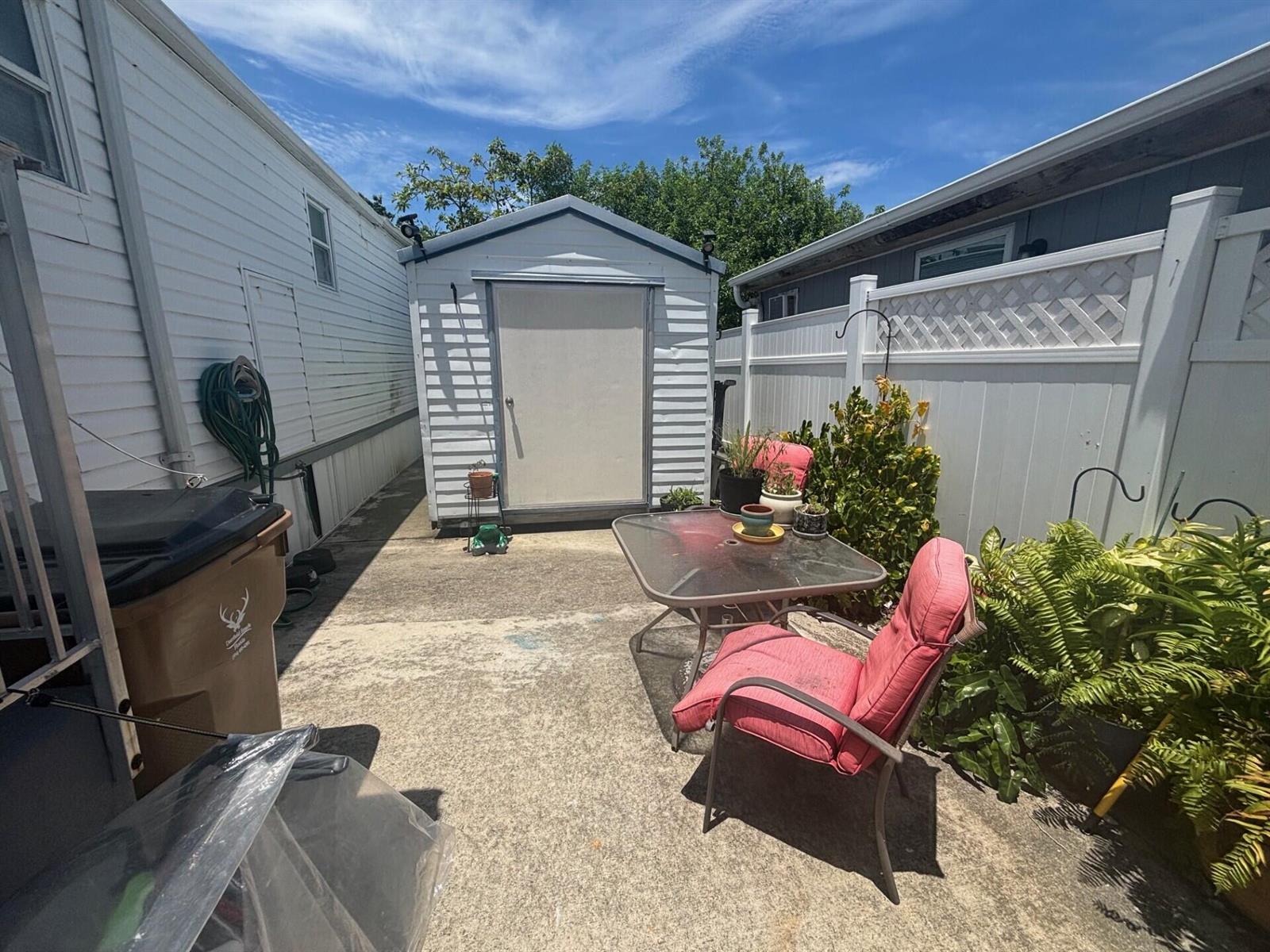 A concrete patio area features a small storage shed, a glass table, and red chairs — 109 NW 50th Street, Deerfield Beach FL 33064, DEERFIELD BEACH, FL