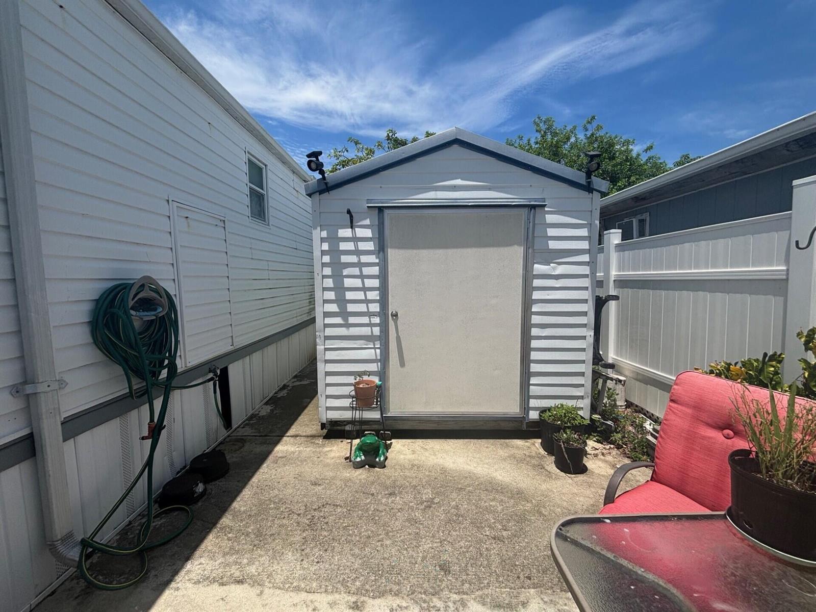 A white storage shed sits on a concrete patio between a house and a fence — 109 NW 50th Street, Deerfield Beach FL 33064, DEERFIELD BEACH, FL