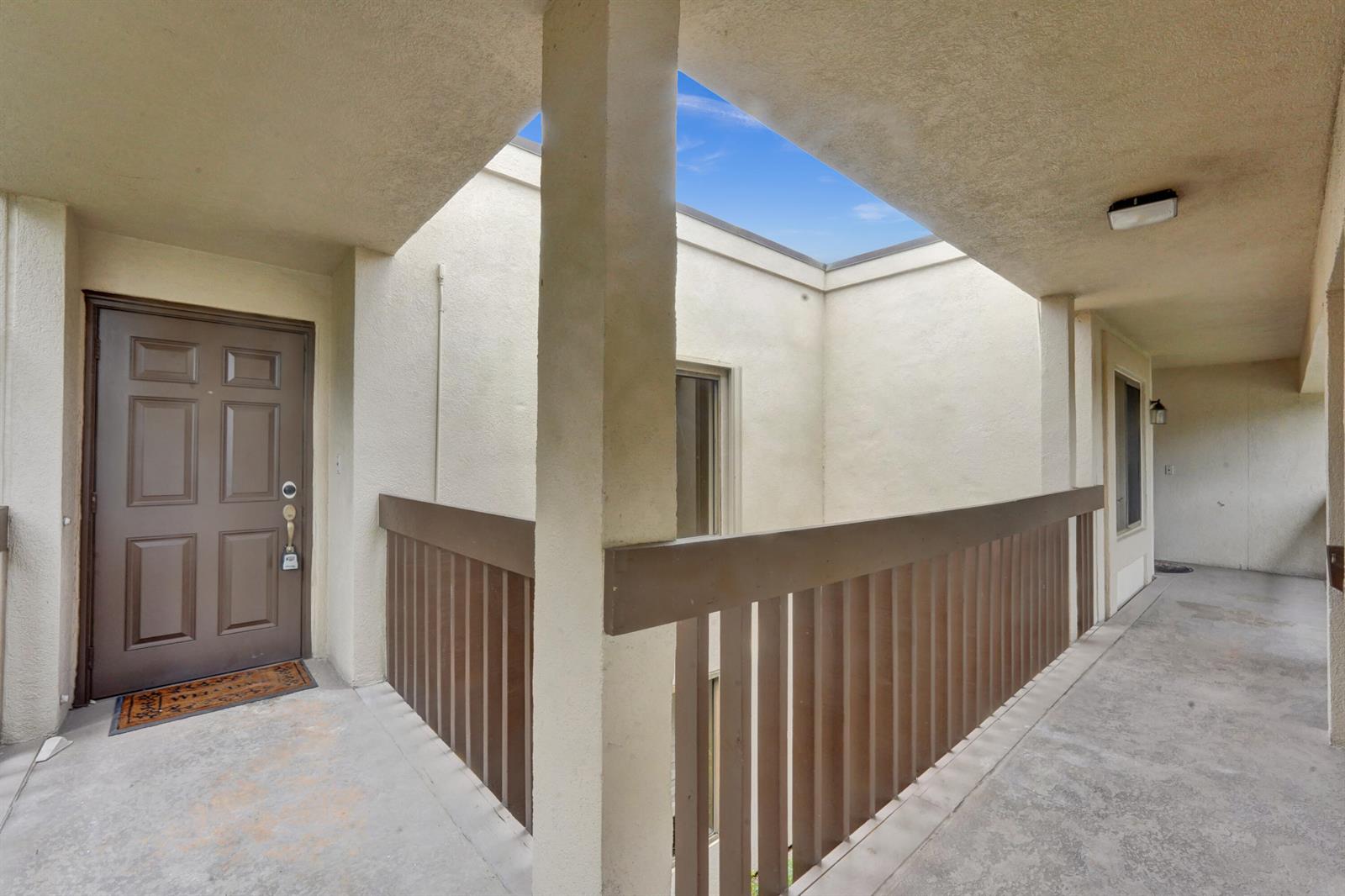 An outdoor walkway with a brown door, wooden railing, and an open-air ceiling — 5306 Cedar Lake Drive # 201, Boynton Beach FL 33437, BOYNTON BEACH, FL