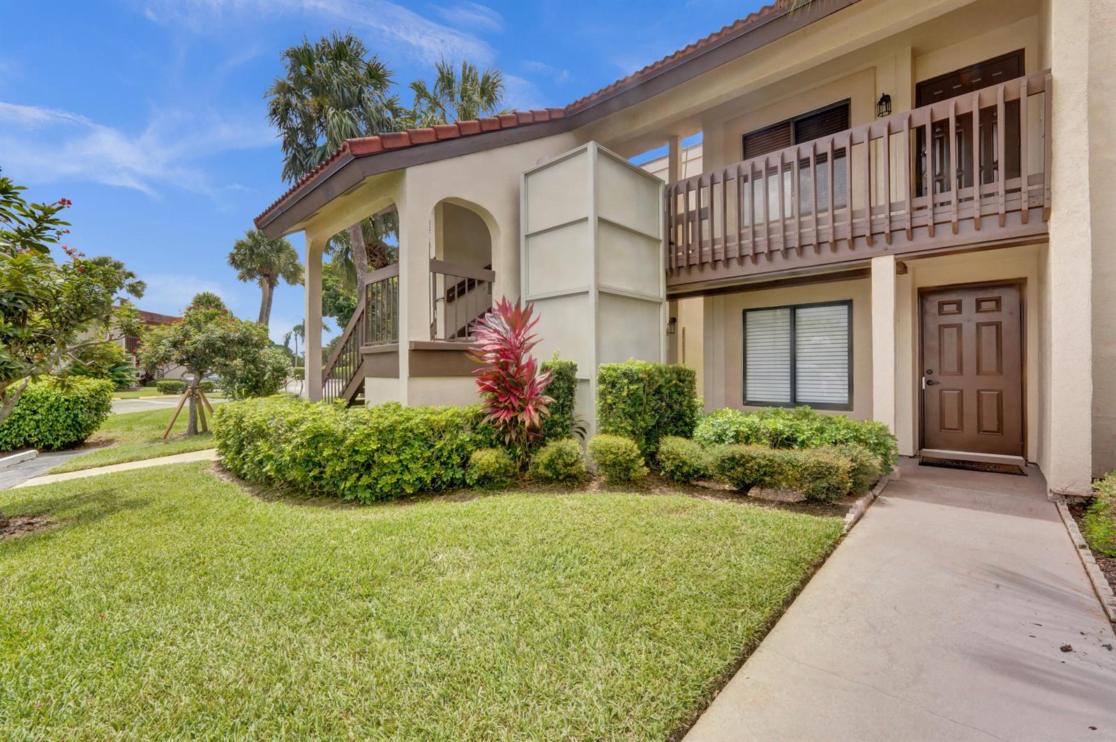 An exterior view of a two-story building with a brown front door and balcony — 5306 Cedar Lake Drive # 201, Boynton Beach FL 33437, BOYNTON BEACH, FL