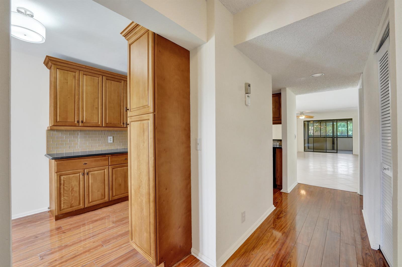 A hallway with wood flooring leads to a kitchen with wooden cabinets and a living area — 5306 Cedar Lake Drive # 201, Boynton Beach FL 33437, BOYNTON BEACH, FL