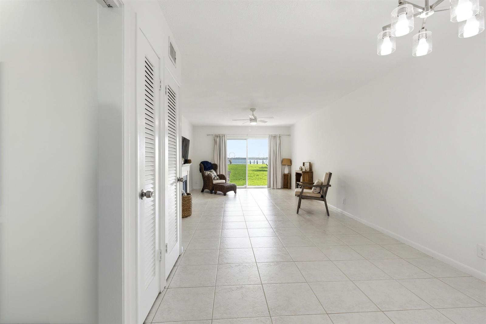 A bright, tiled living room features white walls, louvered closet doors, and a sliding glass door — 311 E Ocean Avenue # 104, Lantana FL 33462, LANTANA, FL