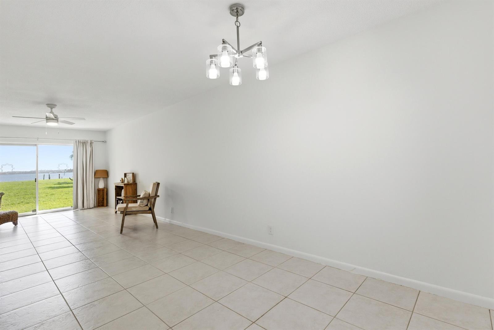 A bright, tiled dining area features a modern chandelier and a sliding door to water — 311 E Ocean Avenue # 104, Lantana FL 33462, LANTANA, FL