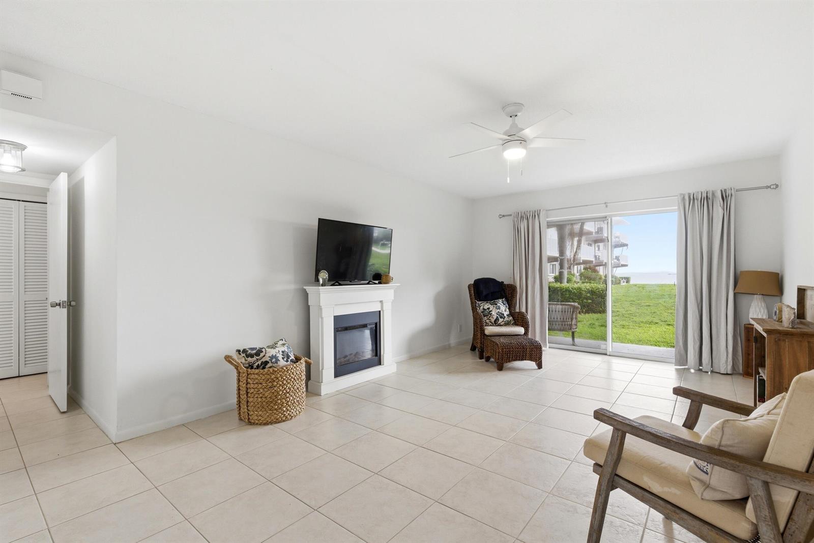 A living room features tile flooring, a fireplace with a television, and sliding glass doors — 311 E Ocean Avenue # 104, Lantana FL 33462, LANTANA, FL