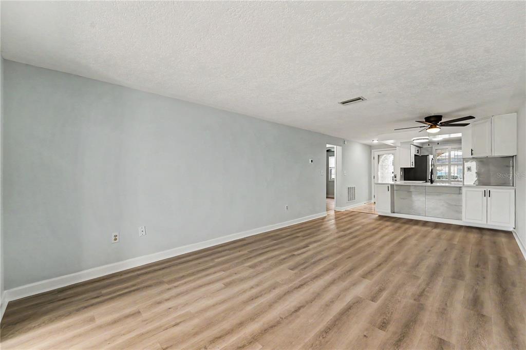 An open-concept living area features light gray walls, wood-look flooring, and a white kitchen — 4247 STRATFORD DRIVE, NEW PORT RICHEY, FL