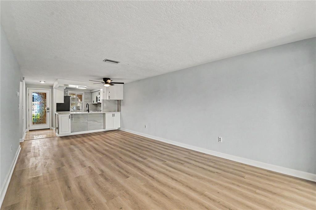 An open-concept living area features light wood-look flooring, gray walls, and an adjacent kitchen — 4247 STRATFORD DRIVE, NEW PORT RICHEY, FL